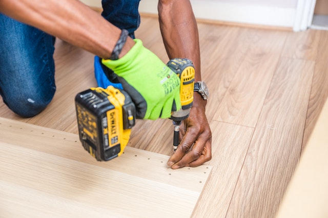 person wearing green work glove drilling into a piece of wood